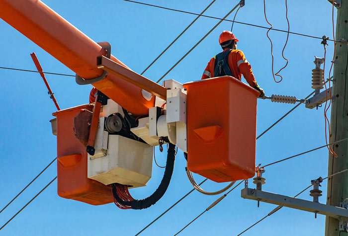 Construction man in a cherry picker, performing aerial inspection on utility cables